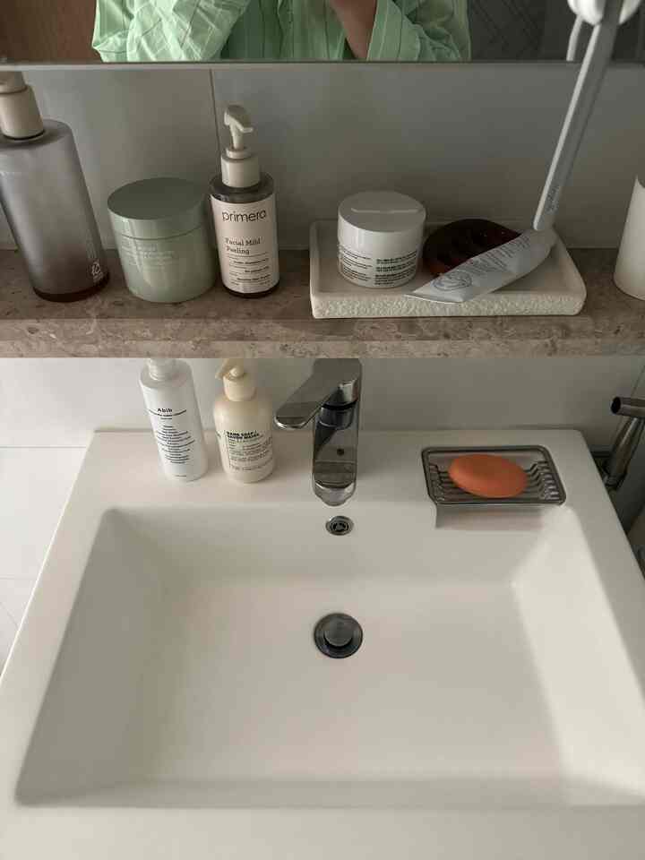 清潔感のある白い色調のバスルーム洗面台と、その上の棚に整然と並べられた浴室用品