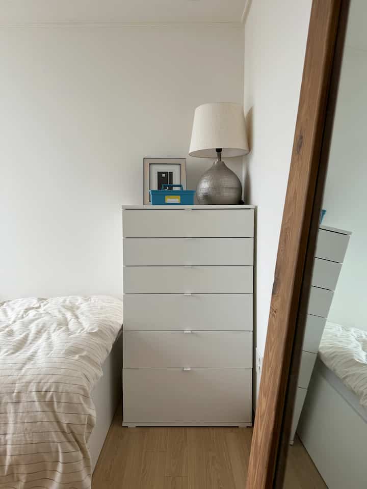 白と木目調が調和する狭い寝室、収納チェストとベッドが配置された清潔感のある空間