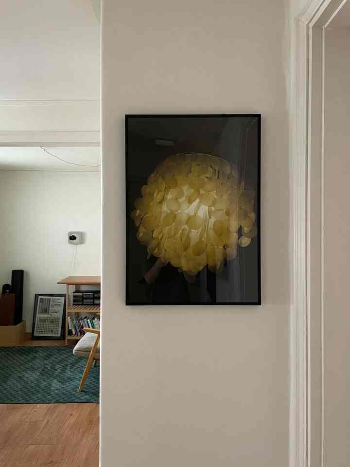 ナチュラルな茶色の床と緑のラグがある玄関の壁に黄色い模様の額縁が掛けられた、雰囲気のあるリビングの一部風景