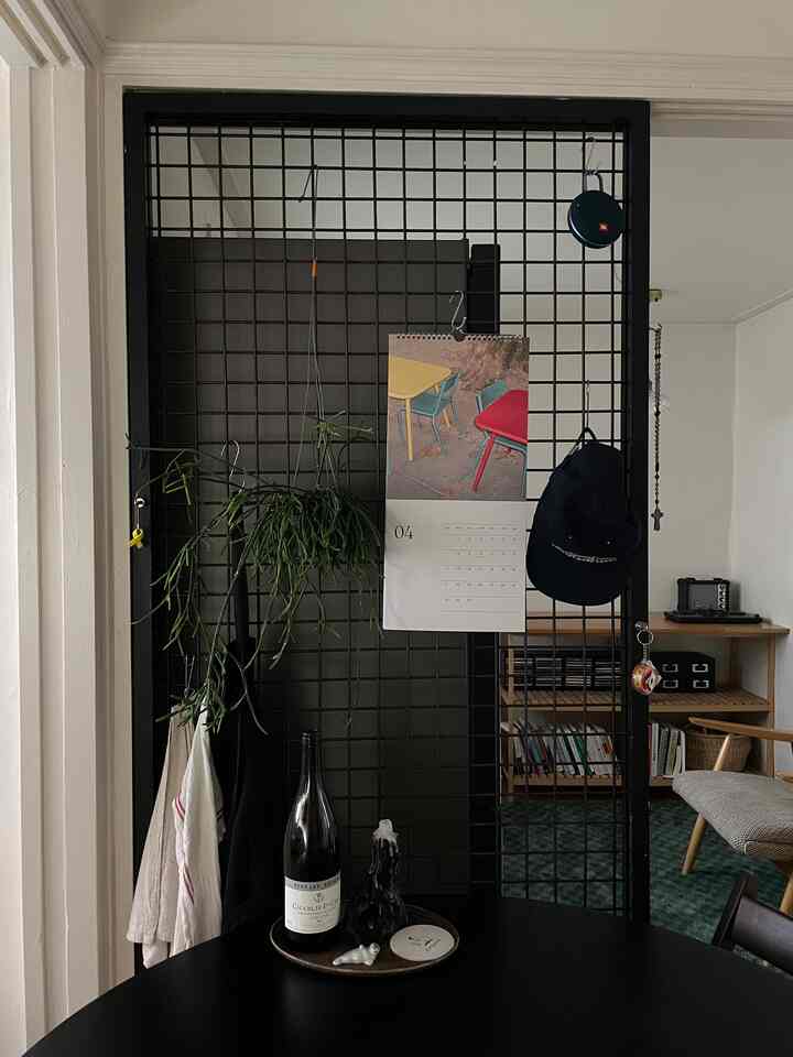 ナチュラルな雰囲気のダイニング空間、黒いメタルグリッドの棚と緑のハンギングプラントが配置された印象的なインテリア