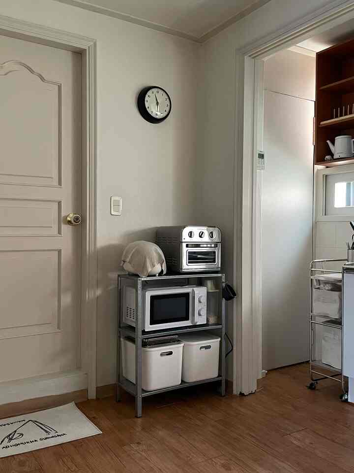 ナチュラルトーンの壁と木製床のキッチン、イケアの金属棚にミニオーブンと電子レンジが配置された実用的な収納スペース