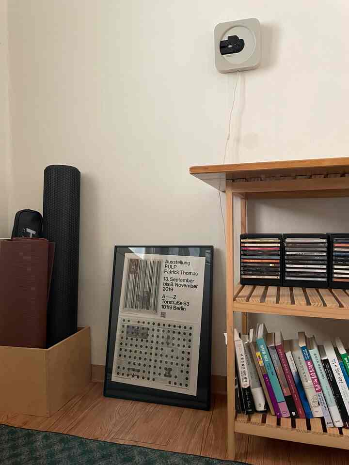 ナチュラルな木目調の棚とヨガマットがある寝室のコーナー、白い壁と額縁が調和した雰囲気のあるインテリア