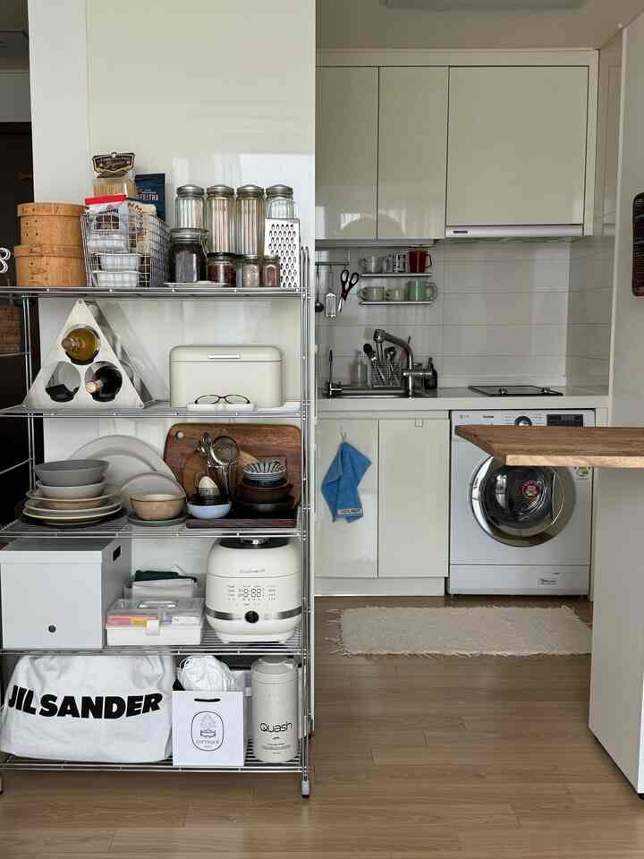 白と木目調が調和したキッチン、ステンレス製のラックに整頓された食器が配置された雰囲気のあるモダンな空間