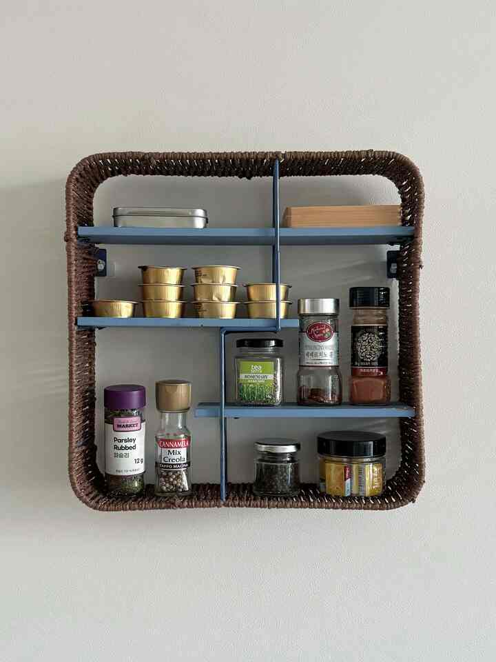 白い壁に青い棚と茶色のラタン縁でスパイスが整然と並んだキッチンスペース