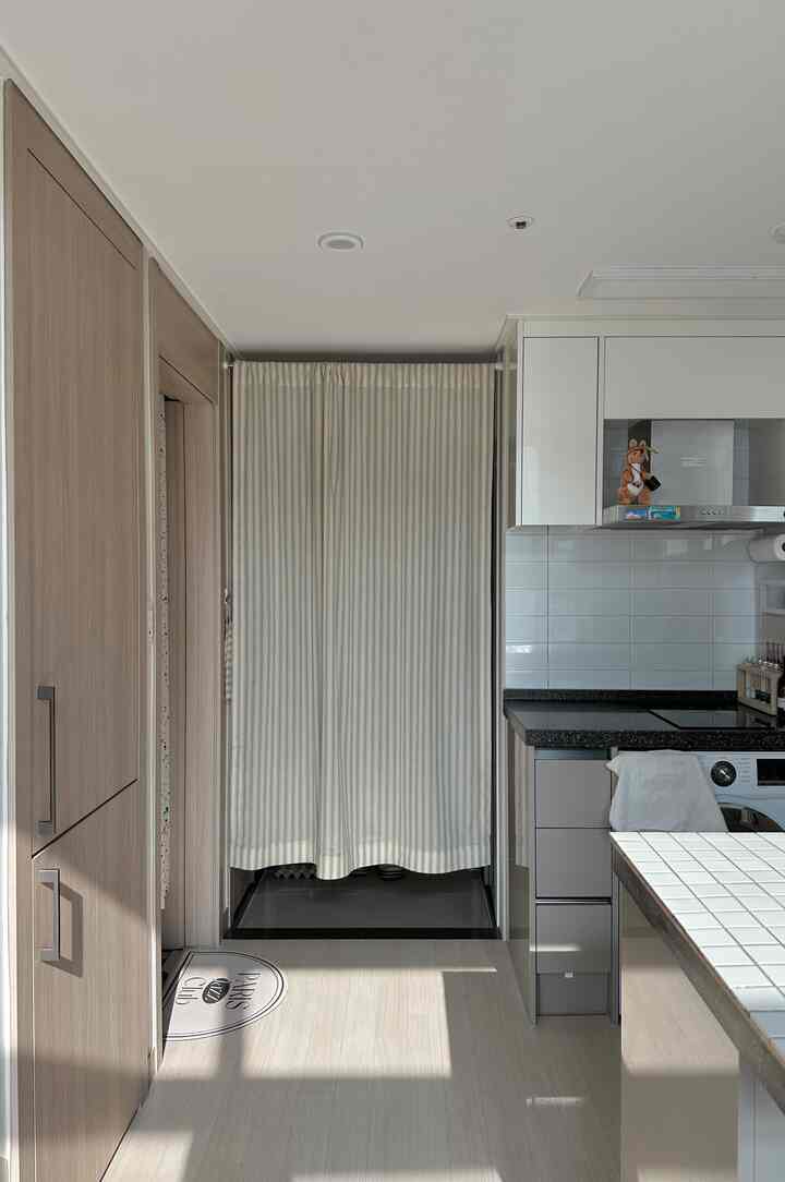 ホワイトとナチュラルトーンのキッチンと玄関スペース、中央にストライプ柄のカーテンが設置されたモダンなインテリア