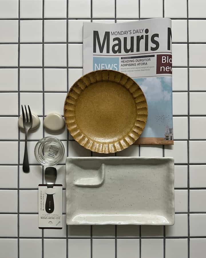 白いタイルのテーブルに配置されたベージュと黄土色の皿があるミニマルなキッチンアクセサリー