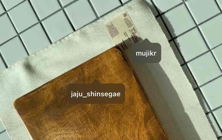 温かみのある木目調と白いタイル床のキッチンスペース、アカシアのまな板と無印良品のランチョンマットが配置された清潔感のあるインテリア