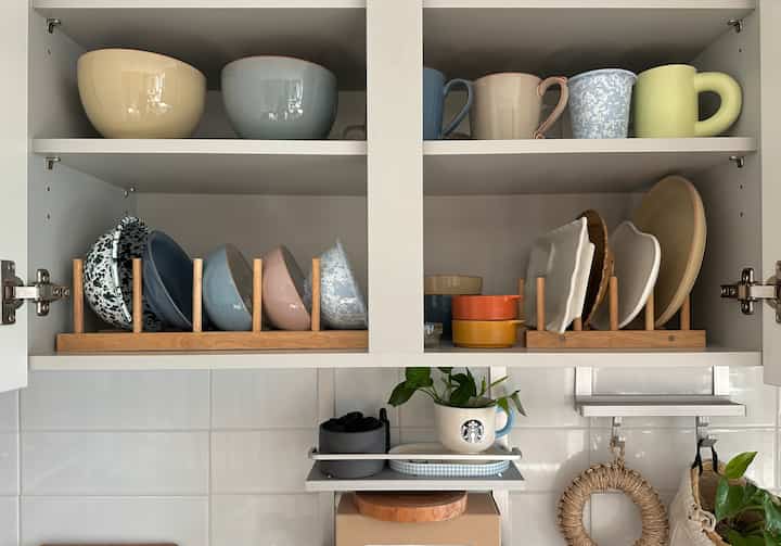 白いキッチン棚に木目調の皿立てと多彩な色のボウルがきれいに配置された雰囲気のあるインテリア