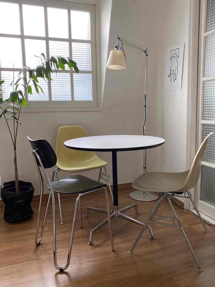 白と木目調が調和したコンパクトなダイニングルーム。ラウンドテーブルと多様な色の椅子、フロアランプが配置されたミニマルなインテリア