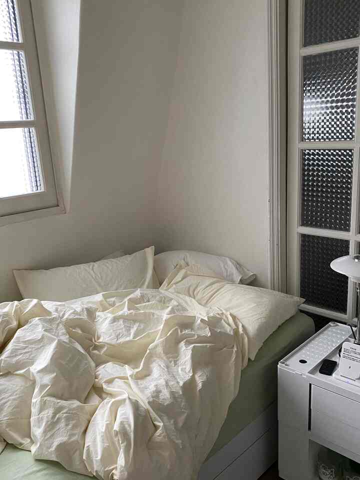 アイボリーとホワイトの色調の寝室、整えられたベッドとナイトテーブルにテーブルランプが配置された落ち着いた雰囲気のインテリア