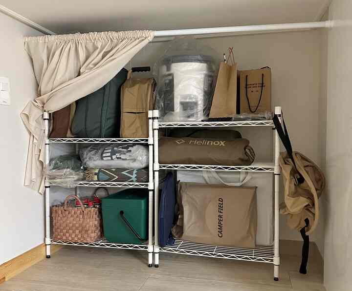 ナチュラルカラーのトーンの小さな空間に金属ラックとベージュのカーテンが配置されたキャンプ用品収納スペース