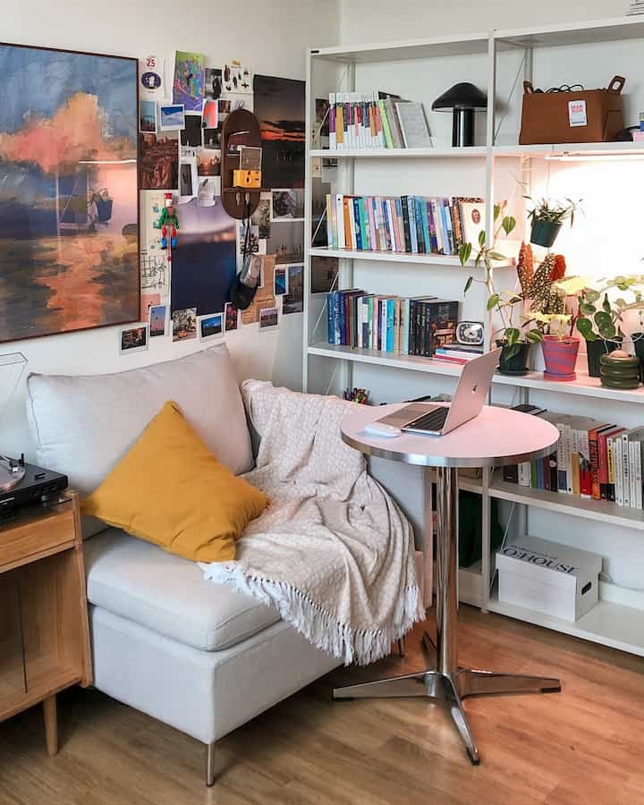 ナチュラルな色調の一人暮らしの書斎、白い本棚とクリーム色のソファ、黄色いクッションと植物が配置された落ち着いた空間