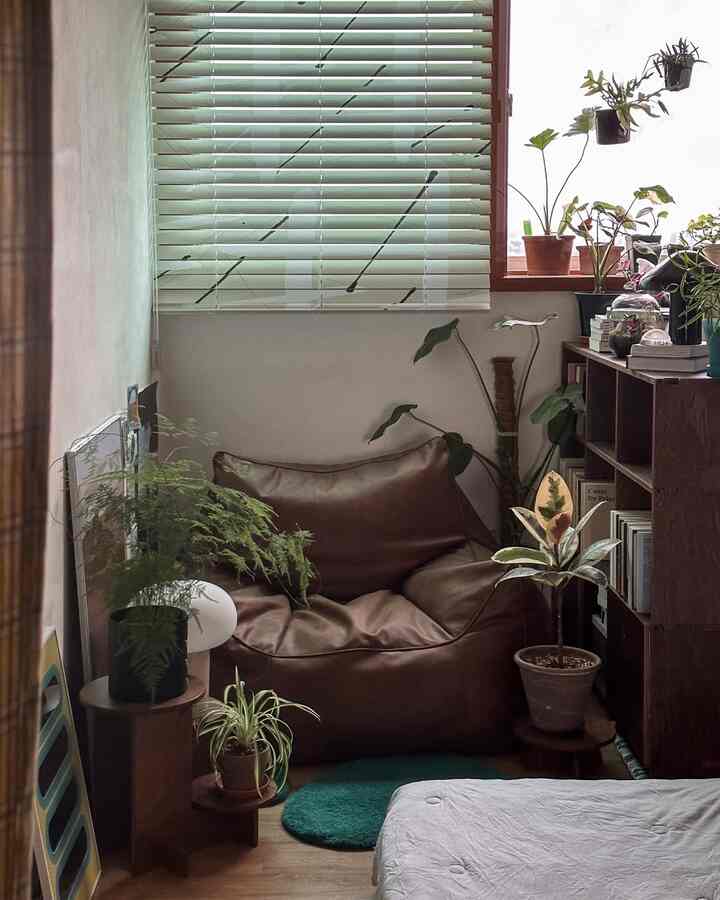 ナチュラルな木目調とブラウンレザーのビーズクッションが置かれた居心地の良いリビング、複数の植物と本棚が自然な雰囲気を演出