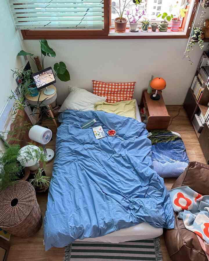 ブルーと木目調の寝室、ベッドとサイドテーブル、複数の植物が配置された落ち着いた自然な雰囲気のあるインテリア