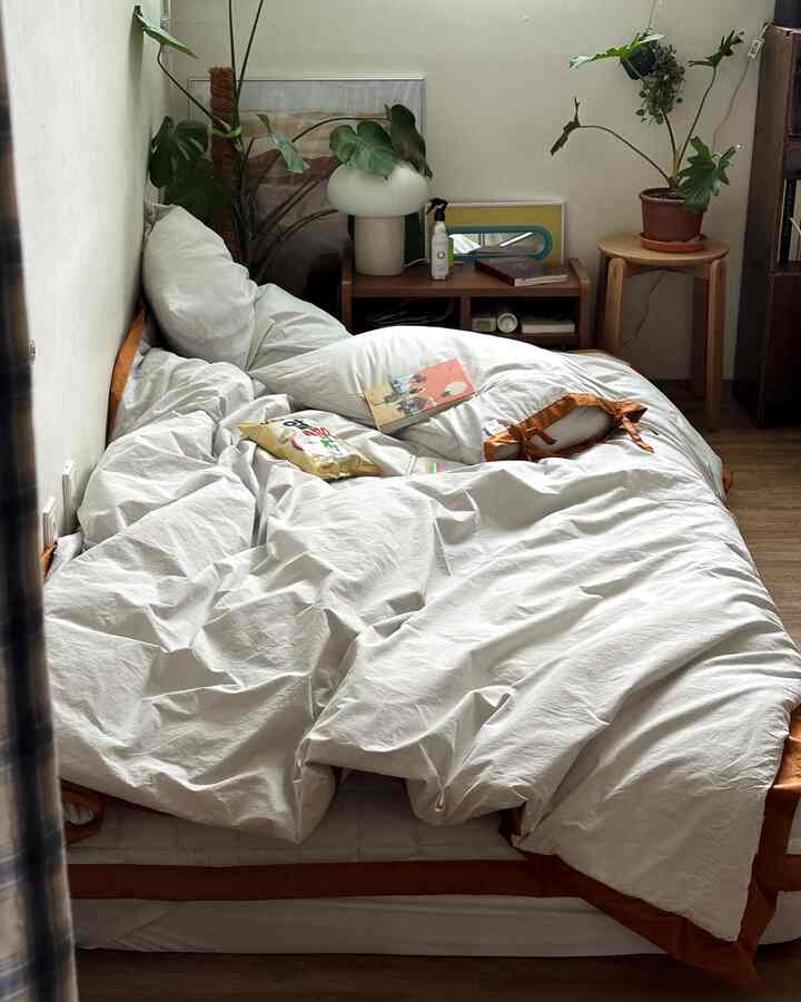 ホワイトとウッドトーンのナチュラルな寝室。ベッドと植物が温かみのある雰囲気を演出