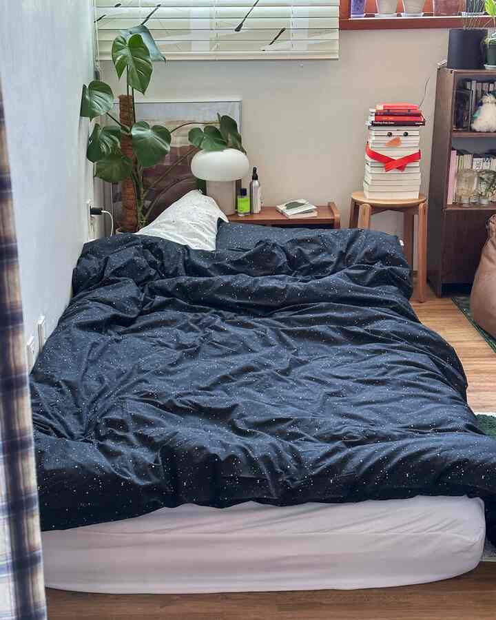 ナチュラルな色調の寝室、暗い星柄の寝具が配置された落ち着いた雰囲気のインテリア