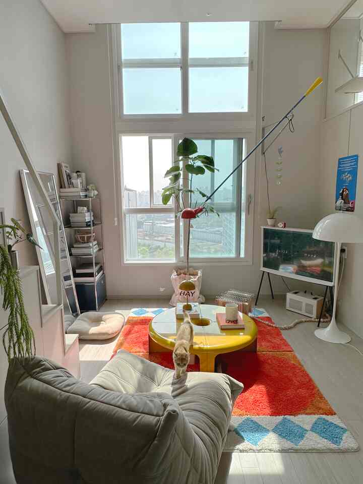 ホワイトとウッドトーンが調和する北欧風リビングルーム、鮮やかなラグと黄色のコーヒーテーブル、アームチェアに猫がいる印象的な空間