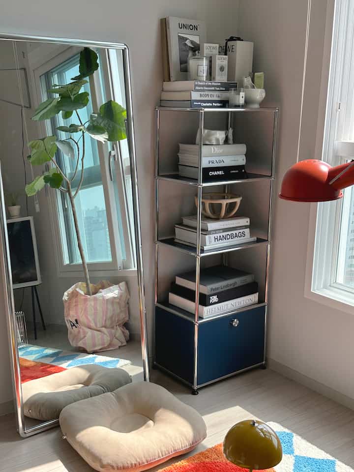 明るい色調の床とネイビーの収納があるリビング、全身鏡とベージュのクッション、赤い壁照明が配置された北欧風の雰囲気のあるインテリア