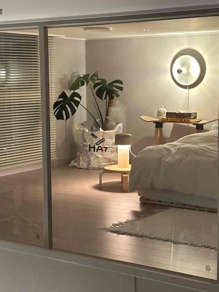 ホワイトとナチュラルウッドトーンの寝室、ミニマルな家具と壁面照明が配置された雰囲気のあるインテリア