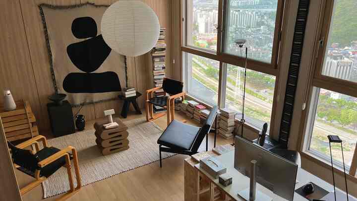 明るい木目調と大きな窓があるホームオフィス兼リビング、机、アームチェア、ラグが配置されたナチュラルモダンな空間