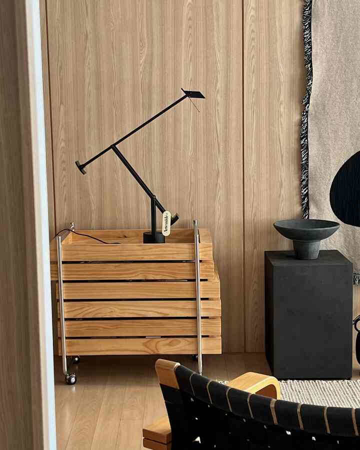 温かみのある木目調の壁と床、ヴィンテージ風の木製トロリーに黒のテーブルランプが配置された居心地の良いリビングインテリア