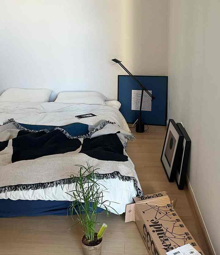 ホワイトとブルーの色調の寝室、中央にベッドとブランケットがあり、右側にスタンドランプと額縁が配置されたナチュラルモダンなインテリア