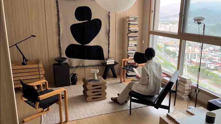 ナチュラルな色調の書斎空間、木目調のアームチェアとラグ、大きな窓のそばで読書をしている様子がある雰囲気のあるインテリア