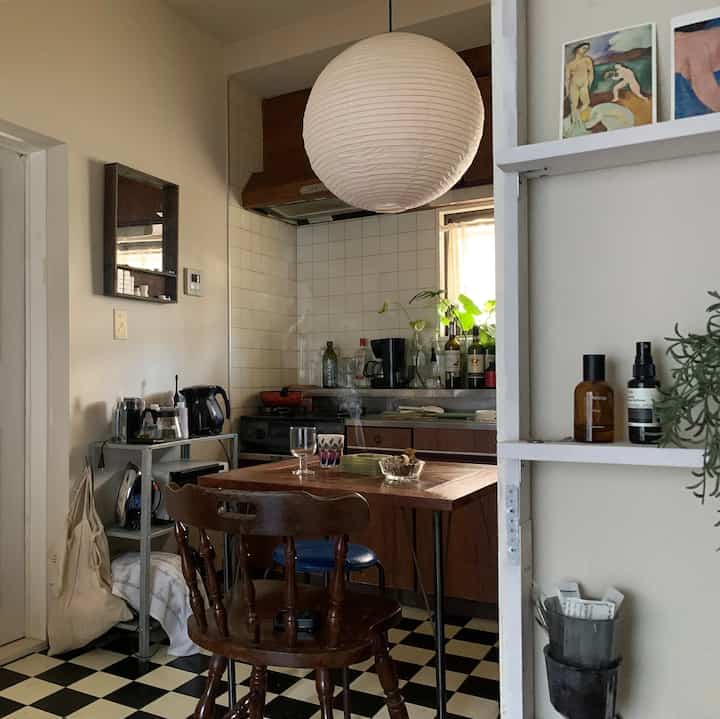 ブラウンとホワイトの色調のダイニング、ヴィンテージの木製ダイニングテーブルと椅子、ペーパーシェードのペンダントライトが配置された温かみのあるキッチン空間