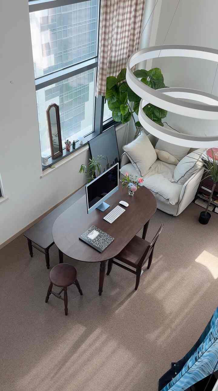 ホワイトとブラウンの色調のワンルームリビング、窓辺に置かれたコンピューターデスクと快適なアームチェアがある清潔なホームオフィス空間