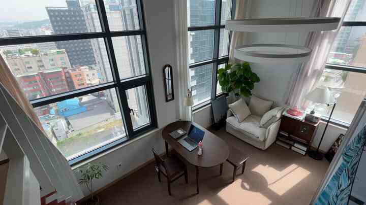 明るいホワイトとブラウン調のロフトワンルームリビング、木製ダイニングテーブルとアイボリーの一人掛けソファが配置された落ち着いた作業空間