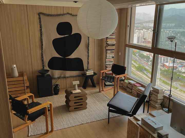 木目調の壁と床の書斎空間、大きな窓際に積まれた本とアームチェアが配置された雰囲気のあるモダンな部屋