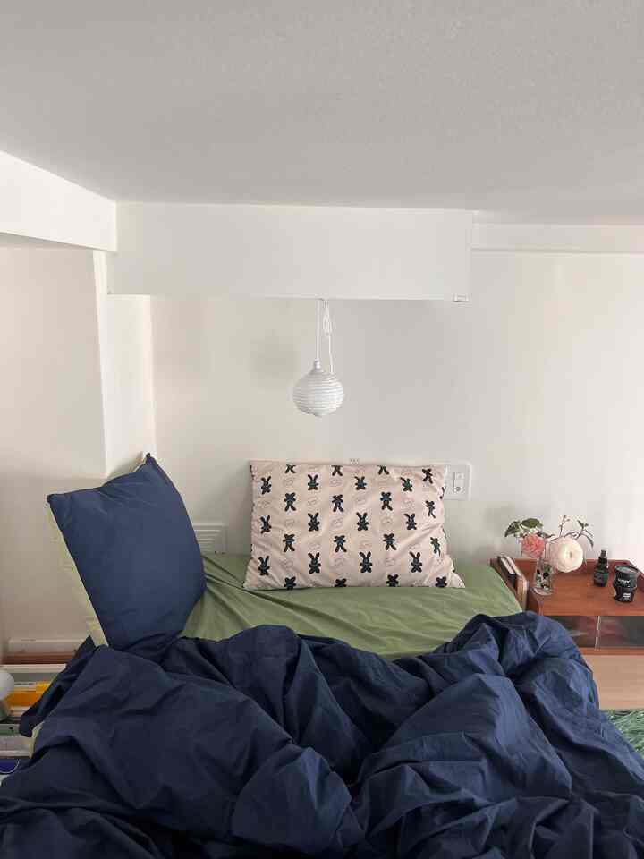 ナチュラルな色調のロフト寝室、低いマットレスと緑の寝具、ネイビーの枕が配置された落ち着いた空間