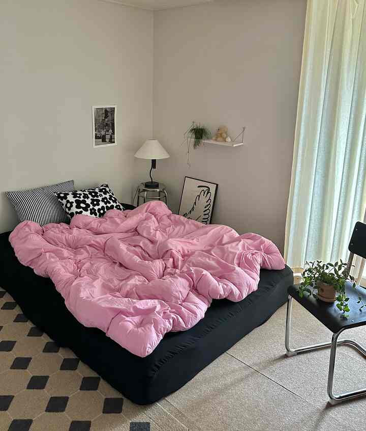 ピンクの寝具と黒いベッドが配置された、清潔感のあるミニマルな寝室のインテリア