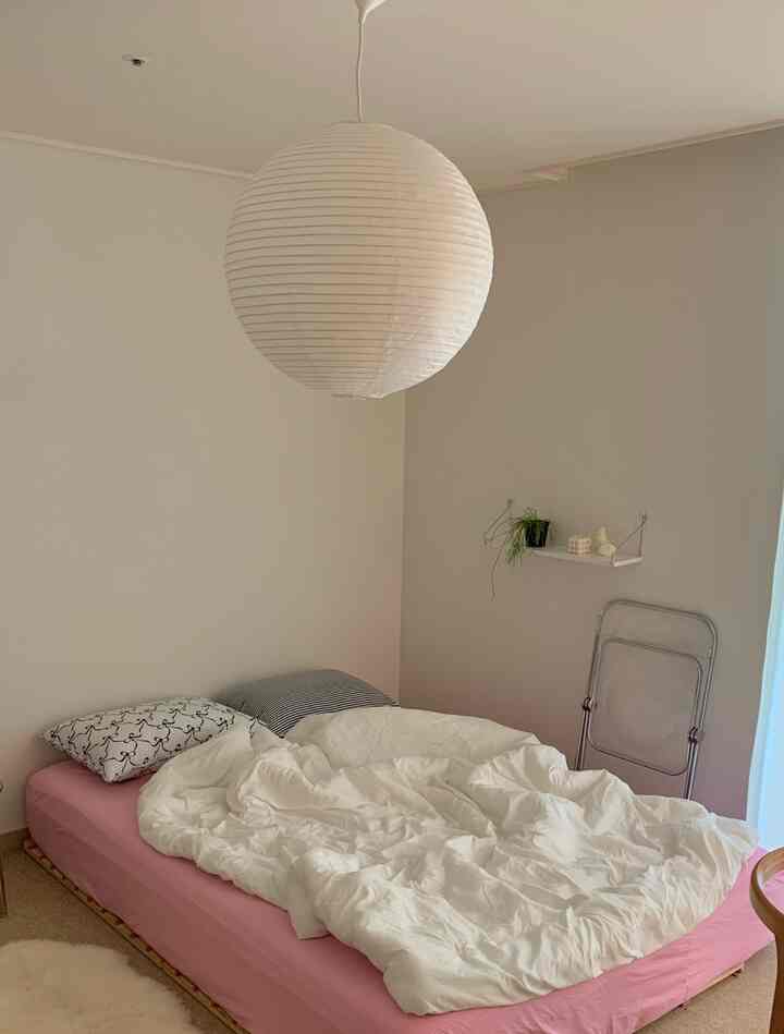 白とピンクのトーンの寝室、ベッドフレームとマットレス、シンプルな照明と棚が配置された雰囲気のあるインテリア