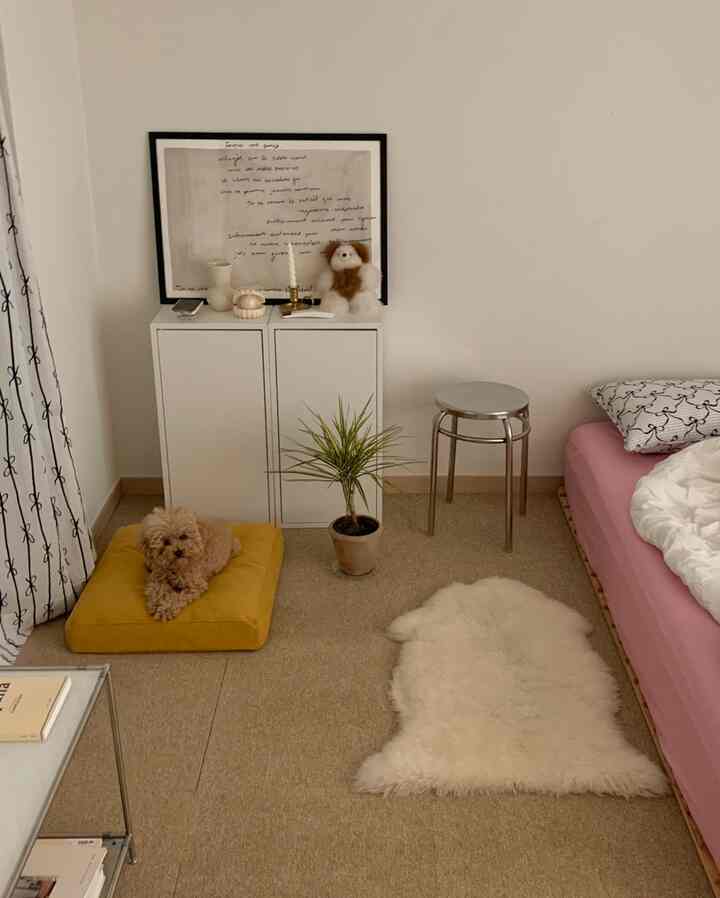アイボリーとベージュの寝室、黄色の犬用クッションとホワイトキャビネット、ピンクの寝具が配置された温かみのある雰囲気のインテリア