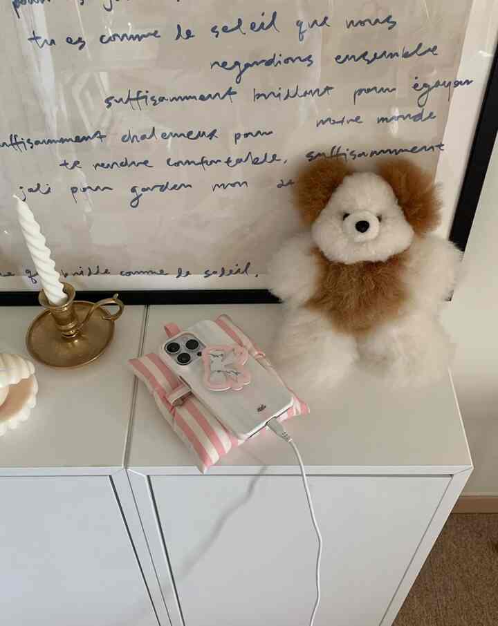 白いキャビネットの上に茶色と白のぬいぐるみ、キャンドルホルダー、スマートフォンが置かれたシンプルで整った空間