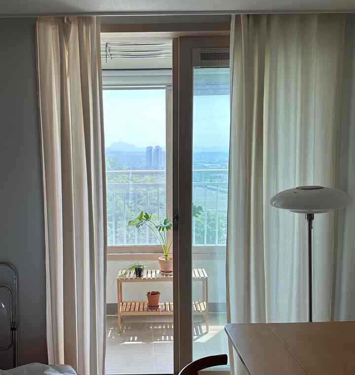 明るいナチュラルトーンのバルコニー、白いカーテンと木製の棚が配置された清潔感のある空間