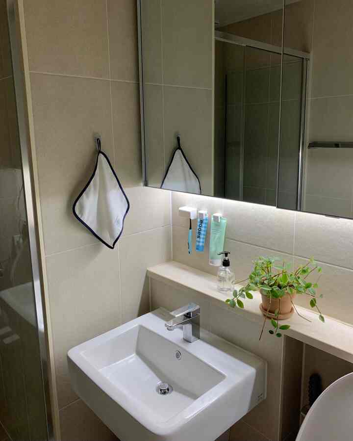白とベージュの色調のバスルーム、洗面台とハンドタオル、緑の植物が配置された清潔感のあるインテリア