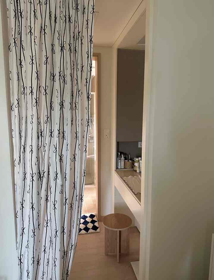 ベージュとナチュラルトーンのウォークインクローゼットとバスルーム、黒いリボン柄のカーテンで仕切られた雰囲気のあるインテリア