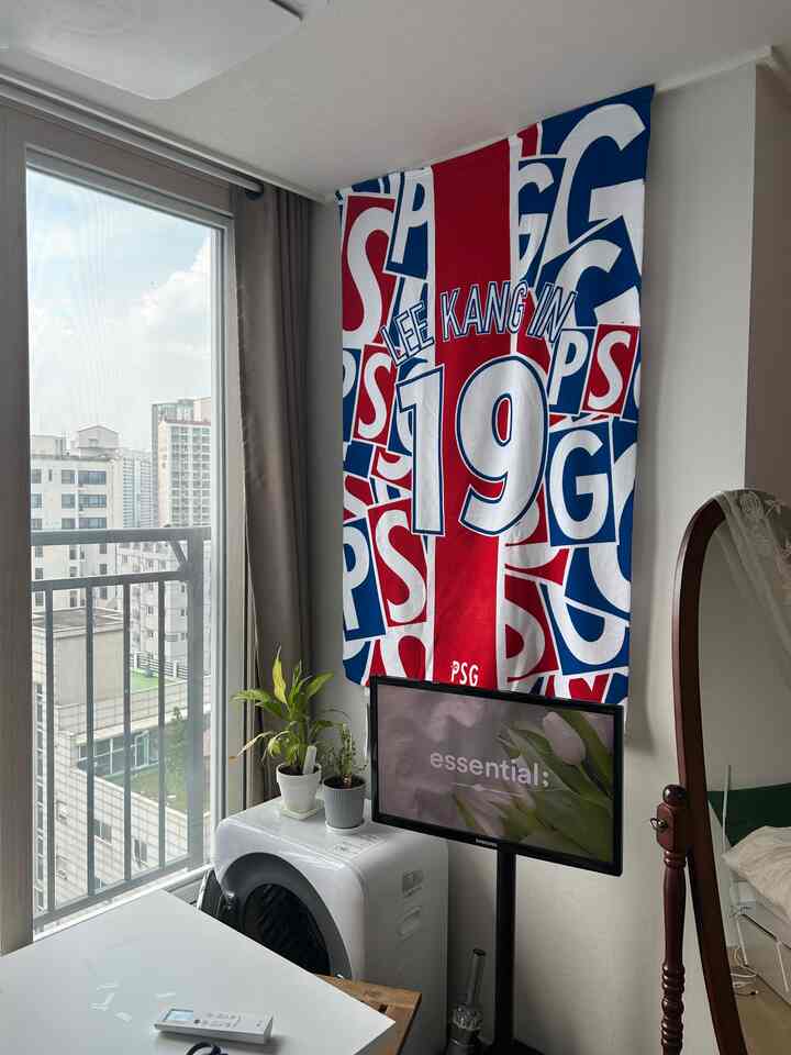 白を基調とした細長いワンルーム空間に、青と赤のアクセントが映える。壁にPSGのタオルを飾り、自然な雰囲気を作る印象的なインテリア