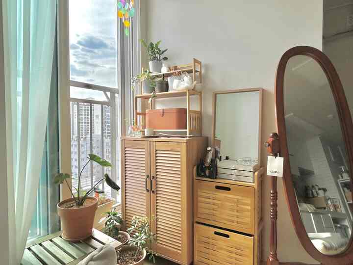 ナチュラルな木目調と植物が調和するベランダ窓辺の収納家具と全身鏡がある落ち着いた空間