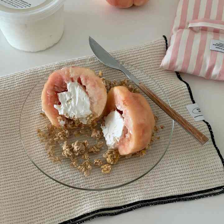 ベージュのテーブルマットの上に置かれた透明なガラスの皿とクリームをのせた桃、木製の柄のナイフが並ぶ雰囲気のあるおうちカフェの印象的な食卓