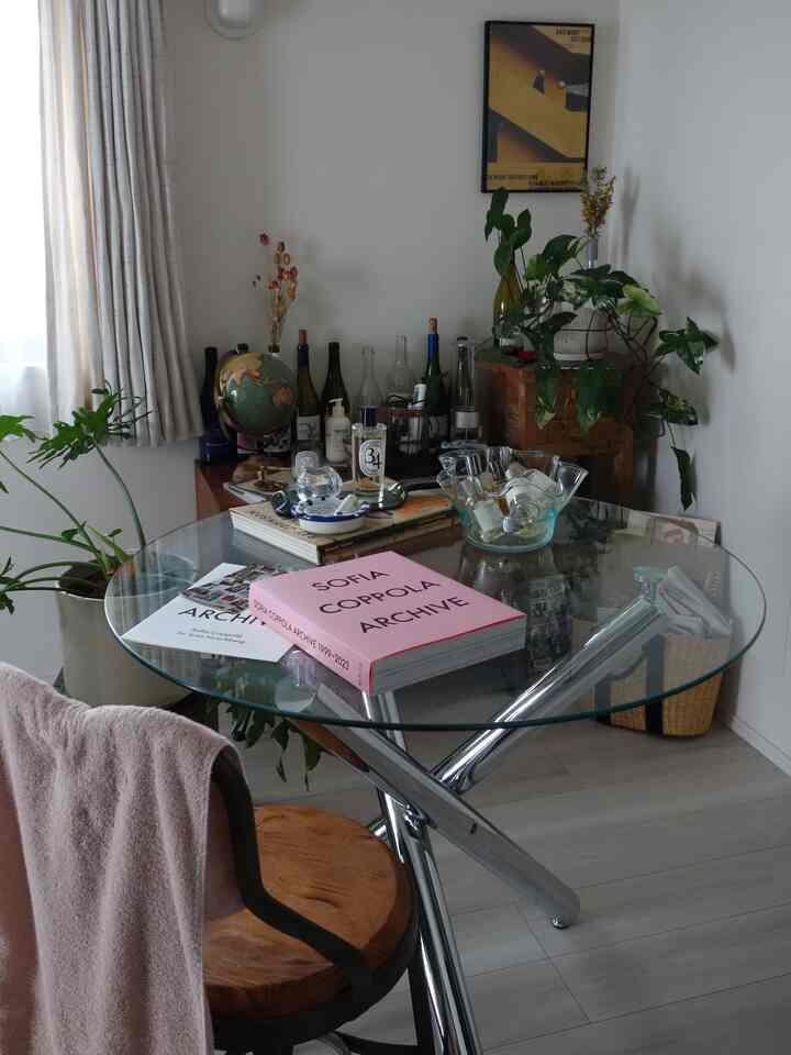 透明なガラスのテーブルと木製の椅子、多様な植物や収納キャビネットが配置された温かみのあるダイニング空間