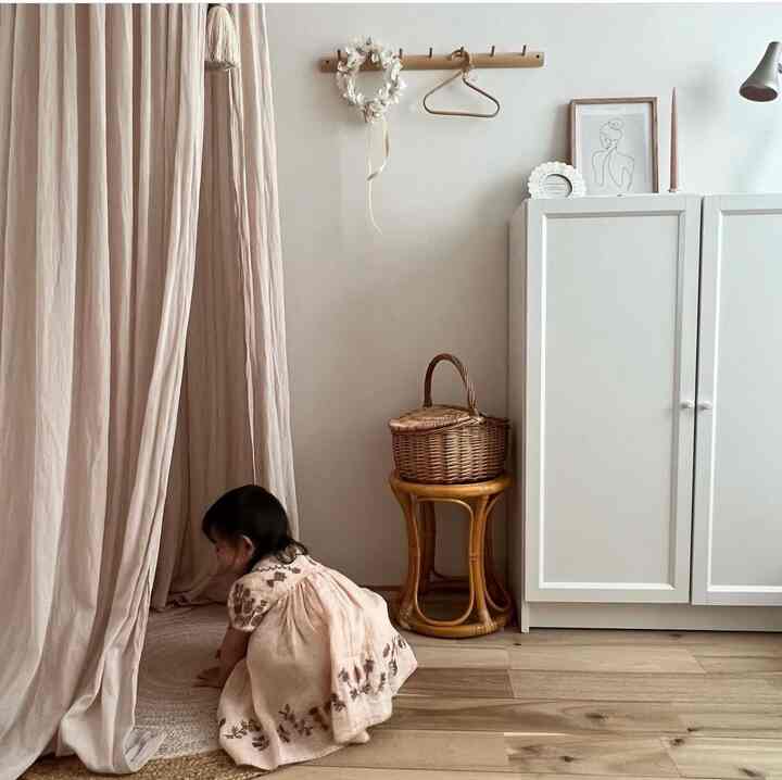 ナチュラルカラーと白を基調とした子供部屋、ベージュのキャノピーと木製スツールが配置された落ち着いた雰囲気のインテリア