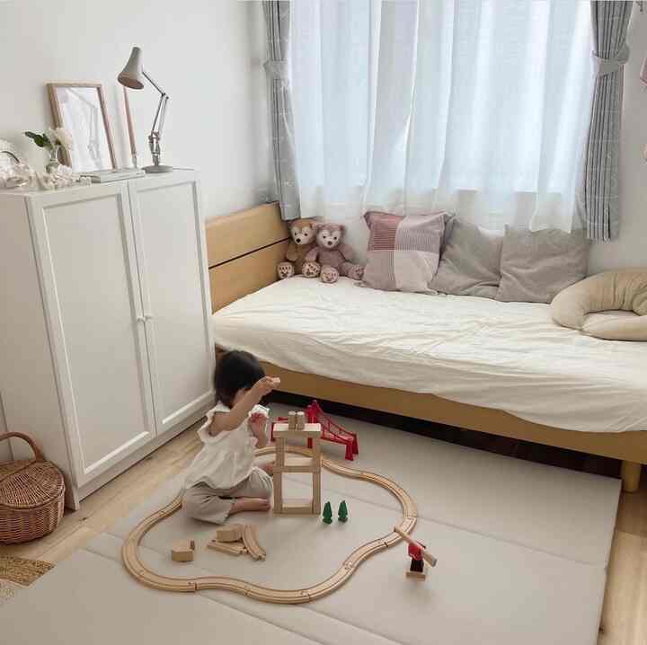 白とナチュラルカラーの子供部屋で、ベッドとラグの上で子供がおもちゃで遊ぶ、雰囲気のあるインテリア
