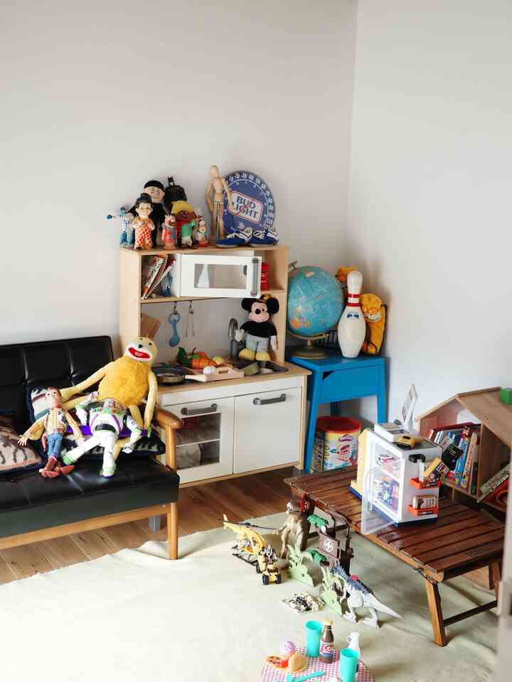 白い壁と黒いソファのある子供と暮らす空間、おもちゃ収納やたくさんの子供用おもちゃが配置された明るく親しみやすい子供部屋