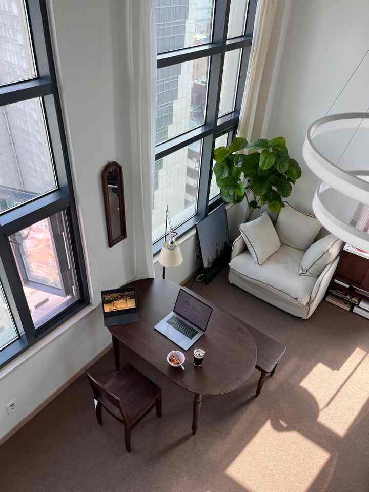 ホワイトとブラウンの色調のリビング、木製ダイニングテーブルと1人掛けソファが配置されたコンパクトで落ち着いた在宅勤務スペース