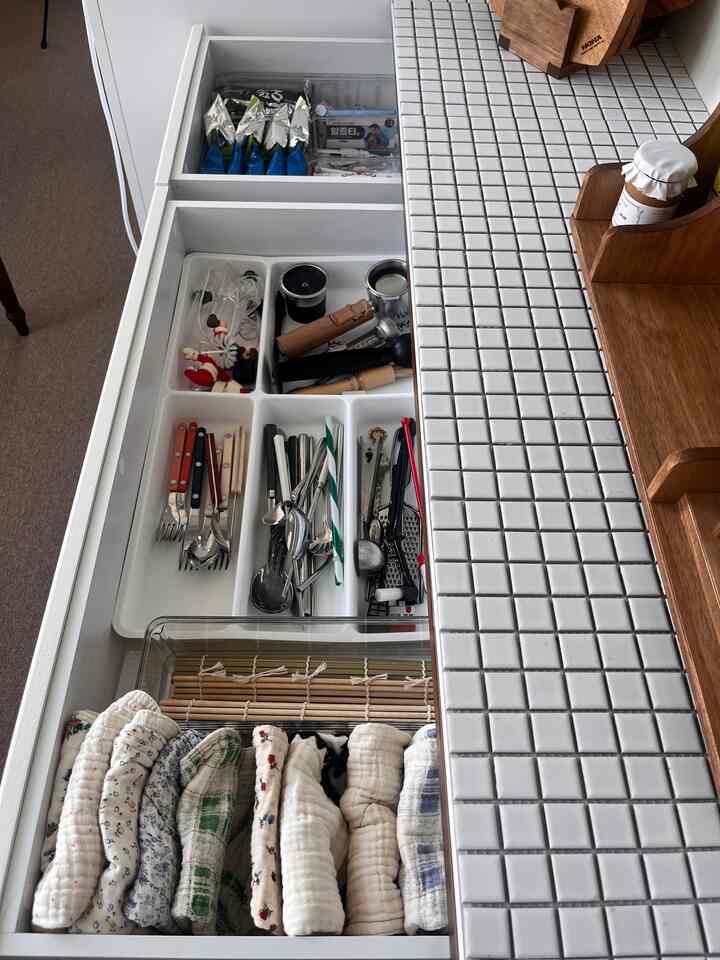 白いタイルの天板とスライド引き出しに整理された多様な調理器具とキッチンタオルが配置された清潔感あるキッチン収納スペース