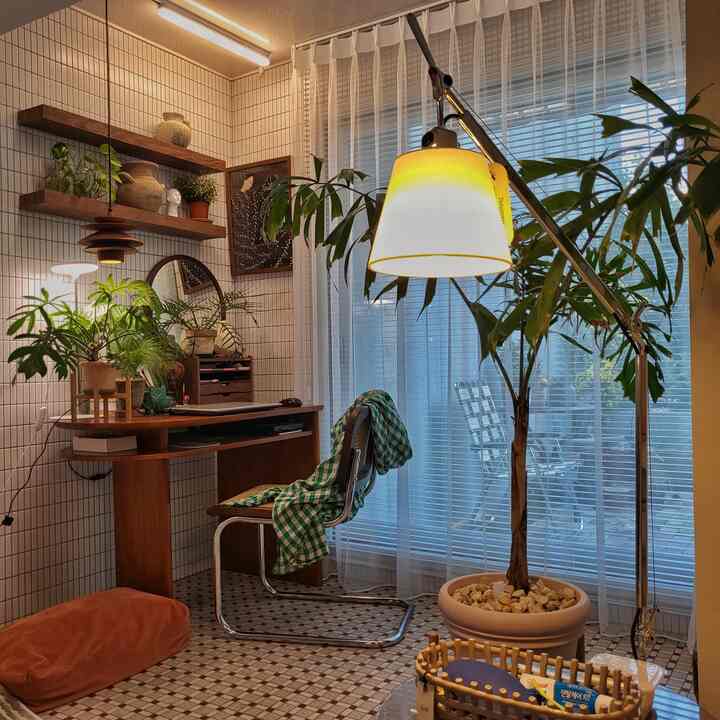 ナチュラルカラーのベランダ兼ホームオフィス、木製の机と多様な植物、フロアランプが配置された落ち着いた空間