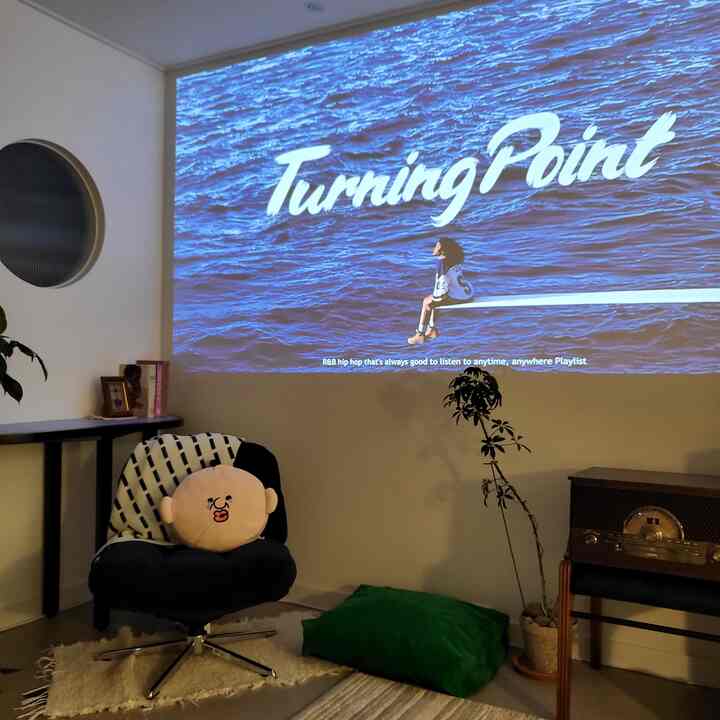 ブルーを基調としたプロジェクター映像が映る小さなモダンなリビング、黒いアームチェアとクッション、植物が配置された落ち着いた空間